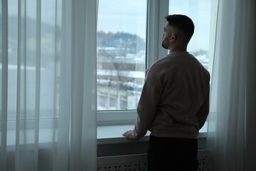 Fototapeta premium Sad man looking at window at home, back view. Space for text