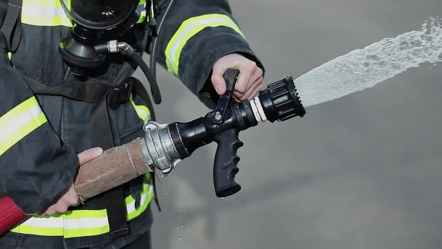 Firefighter in protective suit holds hose and stops water jet by closing nozzle