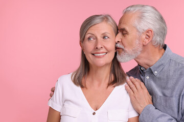 Senior man kissing his beloved woman on pink background, space for text