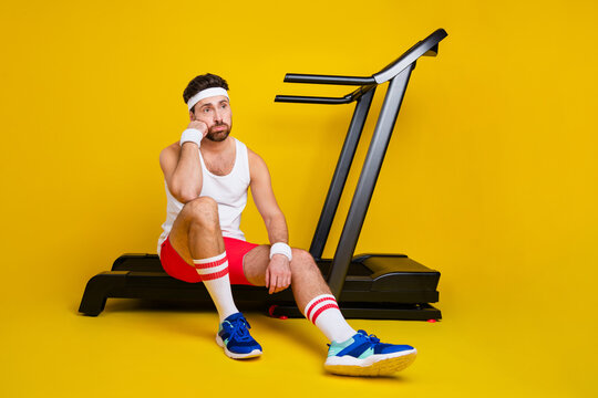 Full length portrait of unsatisfied man sit treadmill brainstorming lack motivation empty space isolated on yellow color background