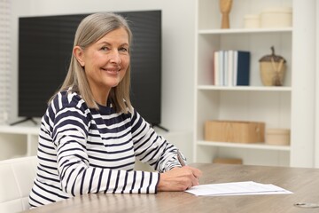 Smiling senior woman signing Last Will and Testament at wooden table indoors. Space for text