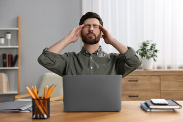 Tired man suffering from headache at workplace in office