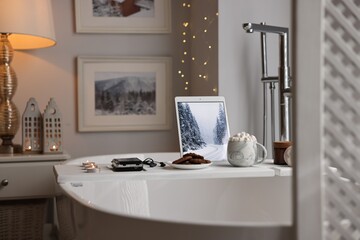 White wooden tray with tablet, cassette player and burning candles on bathtub in bathroom