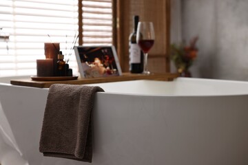 Towel and wooden tray with spa products on bathtub in bathroom, selective focus