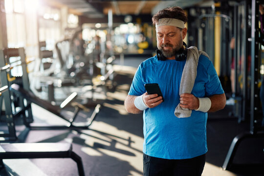 Mature athlete using app on mobile phone while exercising in  gym.