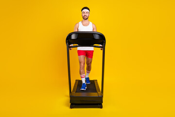 Full length photo of funky cheerful guy activewear walking treadmill empty space isolated yellow...