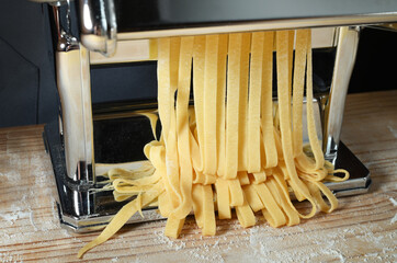 Fresh pasta machine. Egg tagliatelle or fettuccine, closeup. - 730407993