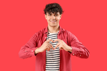 Handsome young man making heart with his hands on red background