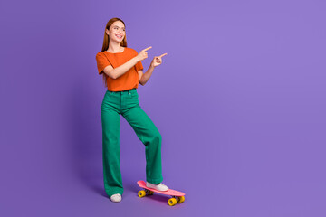 Photo of positive lovely girl wear trendy outfit stand skate presents promo banner empty space isolated on purple color background