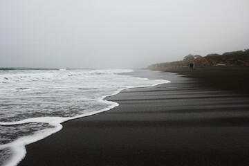 waves rolling on black sand beach in fog
