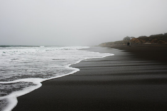 waves rolling on black sand beach in fog