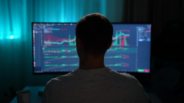 Rear view of unrecognizable financial male analyst using computer with display showing real-time stocks, exchange market charts, drinking coffee. Remote working trader making e-commerce investment.
