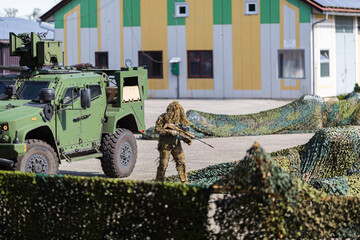 A soldier in camouflage clothing and a green armored military vehicle at a show