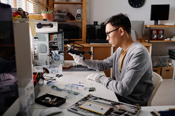 Young caucasian repairman examining broken drone sitting at his desk in workshop