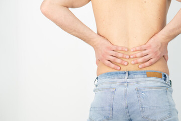 Rear view of a shirtless handsome young man holding his back in pain isolated on white background, muscular attractive man touching his lower back, back pain