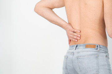 Rear view of a shirtless handsome young man holding his back in pain isolated on white background, muscular attractive man touching his lower back, back pain