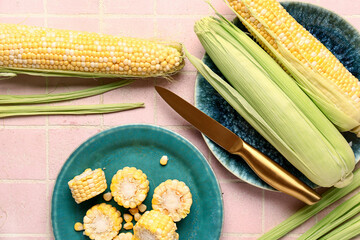 Plates with fresh corn cobs on pink tile background