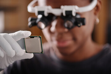 Black woman in glasses with loupes holding CPU and attentively looking at it, focus on CPU