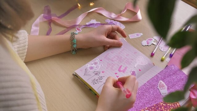 A teenage girl makes scrapbooking, dwawing with pen and fills a diary full of stickers for Valentine's Day. High quality 4k footage