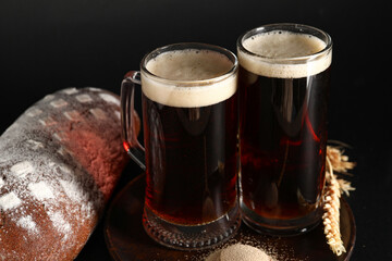 Mugs of tasty kvass and bread on black background