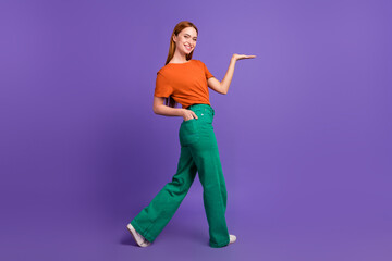 Full body length photo of young smiling girl in green pants demonstrate new collection clothes isolated on purple color background