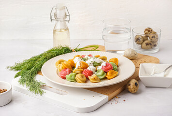Plate of boiled colorful dumplings with sour cream and dill on white background