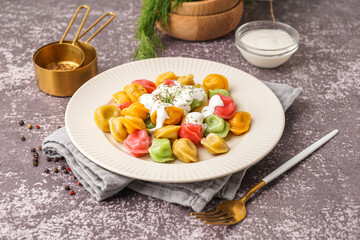 Plate of boiled colorful dumplings with sour cream and dill on dark background