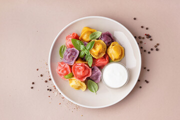 Plate of boiled colorful dumplings with basil and sour cream on beige background