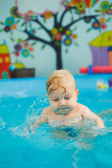 Fototapeta na wymiar Training of a newborn child in a swimming pool. A pool for babies. Child development. A small child learns to swim in the pool