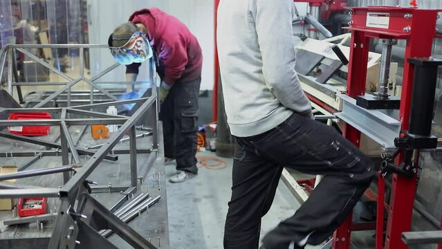  (PR) Two men weld carcase and work on press tool in assembling workshop of DB 527 sport car production company. Slow motion