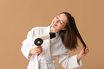 Beautiful woman in bathrobe drying hair after shower on beige background