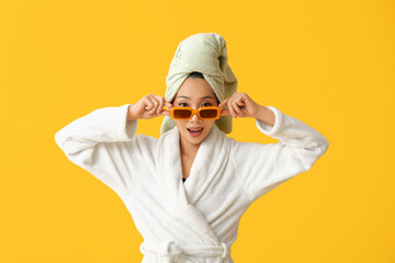 Young Asian woman in sunglasses after shower on yellow background