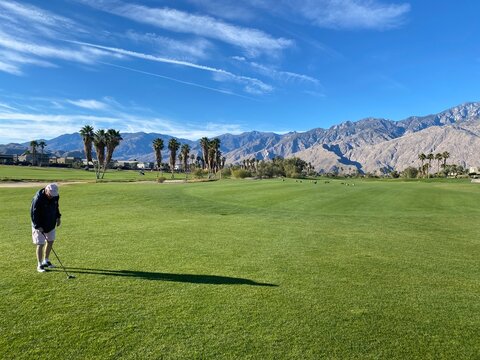 A senior man on the fairway about to hit a golf ball on a beautiful day in Palm Springs, California, USA, on a beautiful sunny winter day with the mountains in the background.