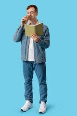 Fototapeta premium Young man reading book and drinking coffee on color background