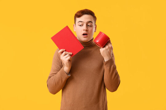 Emotional young man holding book and mug on yellow background