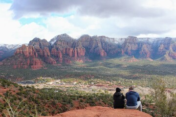A couple sitting at the Airport Mesa Sedona vortex overlooking Sedona, Arizona on a beautiful sunny winter day, with the red rocks and mountains in the background