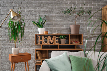Shelf unit with green plants and books near grey brick wall in living room