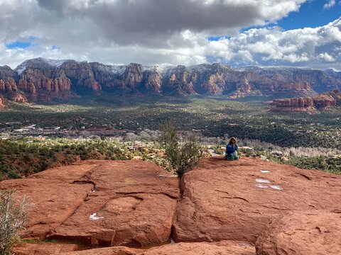 A young girl sitting at the Airport Mesa Sedona vortex overlooking Sedona, Arizona on a beautiful sunny winter day, with the red rocks and mountains in the background