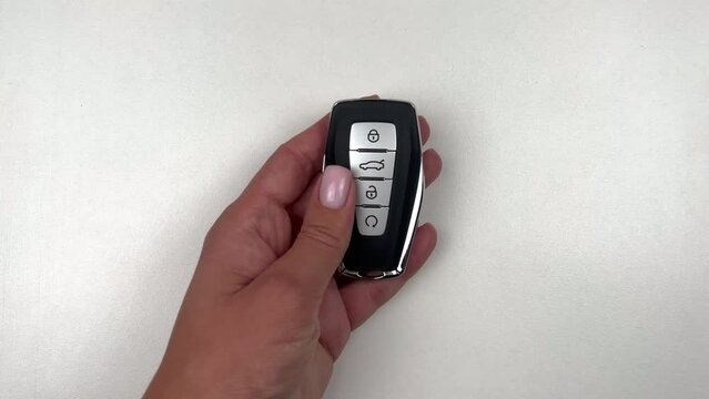 A black car key with metal inserts and automatic buttons is taken by the hand of a person of European appearance, runs his fingers over the buttons and takes the key on a white background. High