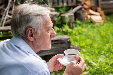Elderly man sipping tea in a backyard, pile of wood in background, with a focus on relaxation and...