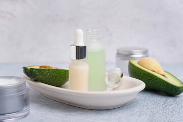Fresh avocado and bottles of essential oil on light background, closeup