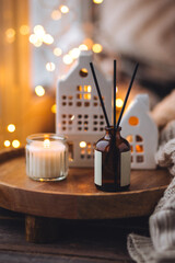 Aroma diffuser, burning candle, Christmas perfume on wooden bamboo tray, knitted sweater. Cozy home decor, hygge and aromatherapy concept. Comfortable atmosphere, Scandinavian decor.