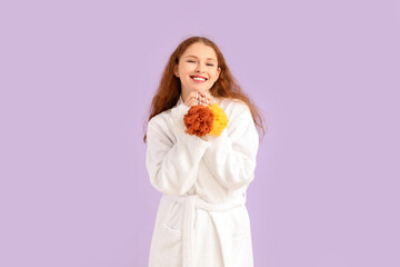 Young woman in bathrobe with loofahs on lilac background