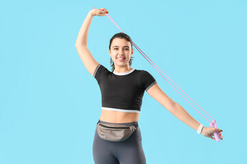 Young woman in sportswear with skipping rope on blue background