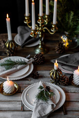 Beautiful table setting for family Christmas dinner at home. Cozy atmosphere, candlelight. Wine glasses, vintage chandelier, elegant interior. Fir tree branches, wooden furniture, dark, bokeh