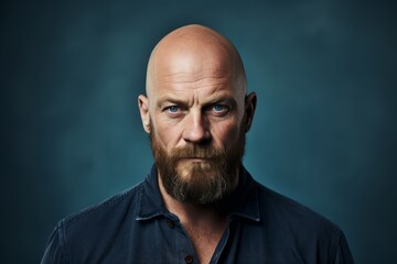 Portrait of a bald man with a long beard and mustache in a blue shirt