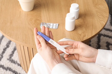 Woman with pregnancy test and pills at home, closeup