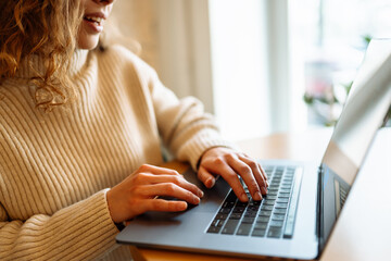 Fototapeta premium Close-up of hands working on a laptop keyboard. Home working and browsing concept in a cozy atmosphere. Freelance, online course. Shopping online. Cyber security concept