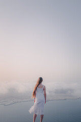 Fototapeta na wymiar Young woman in white long dress looks in direction to island during the sunset at Mirador Del Rio, Lanzarote