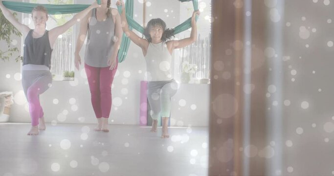 Animation of white light spots over diverse female instructor and teenage girls doing aerial yoga